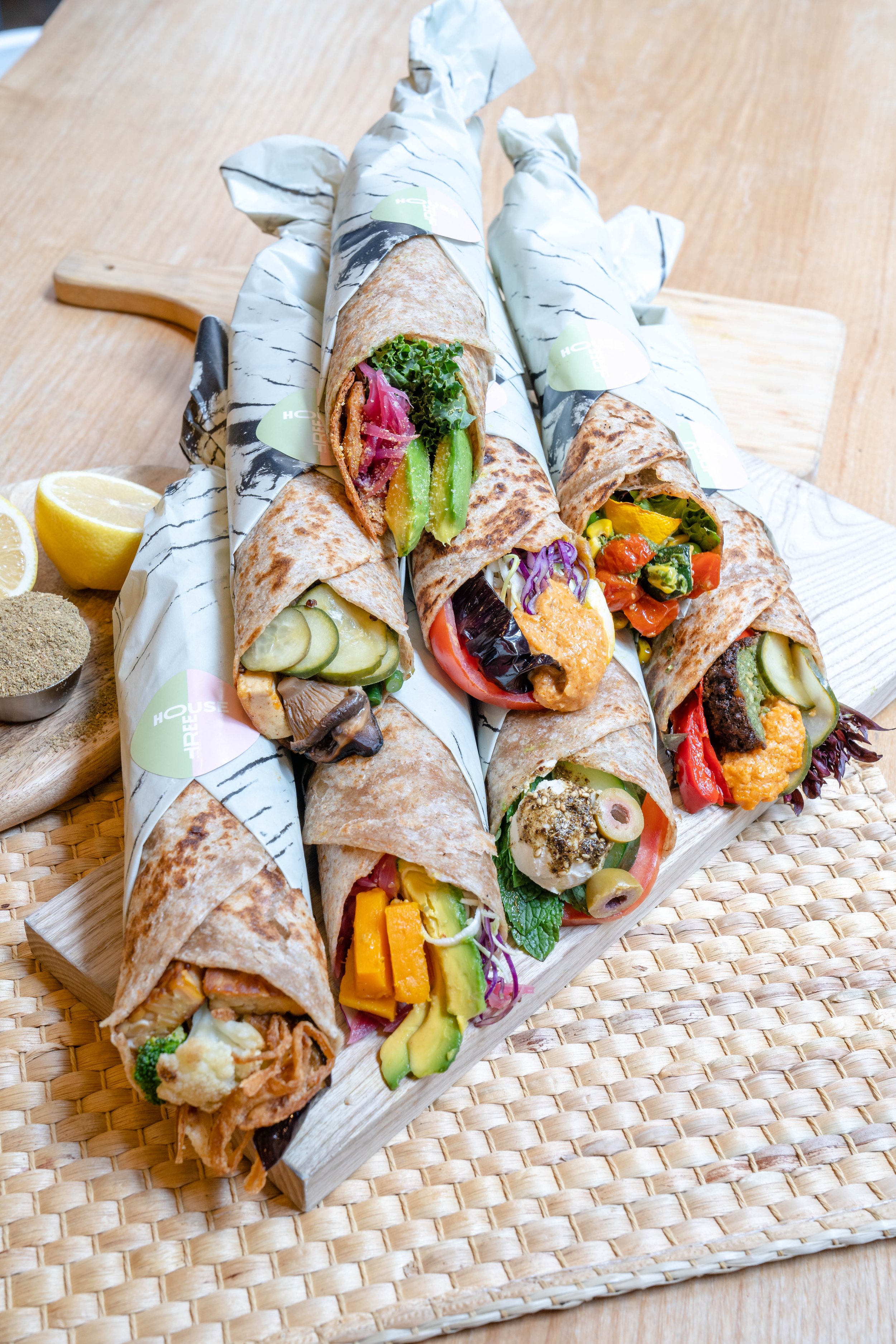 Assorted wraps filled with colorful vegetables, wrapped in decorative paper, placed on a wooden board.