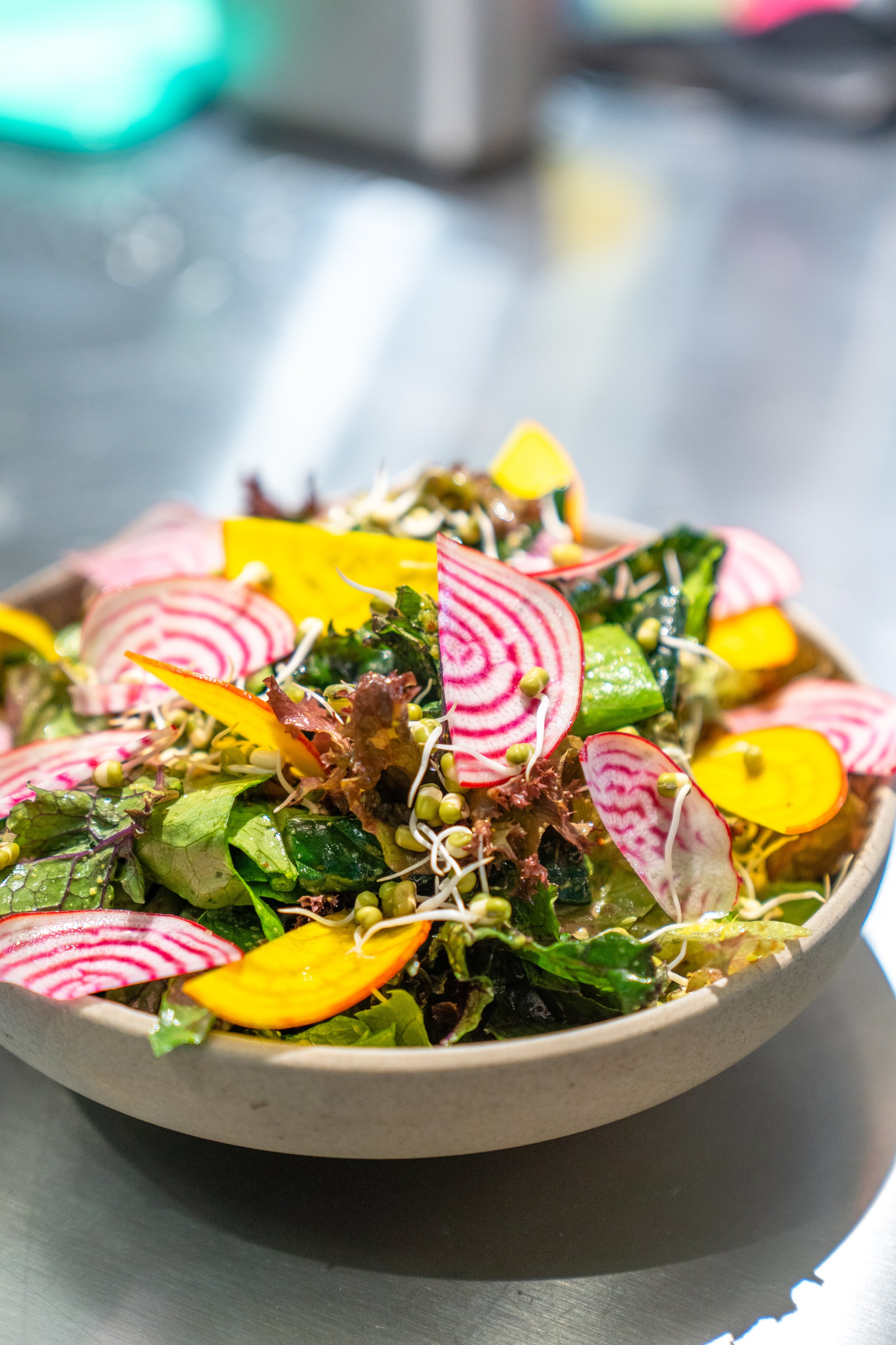 Colorful vegetable salad with greens, sliced chioggia beets, yellow beets, sprouts, and seeds in a bowl.